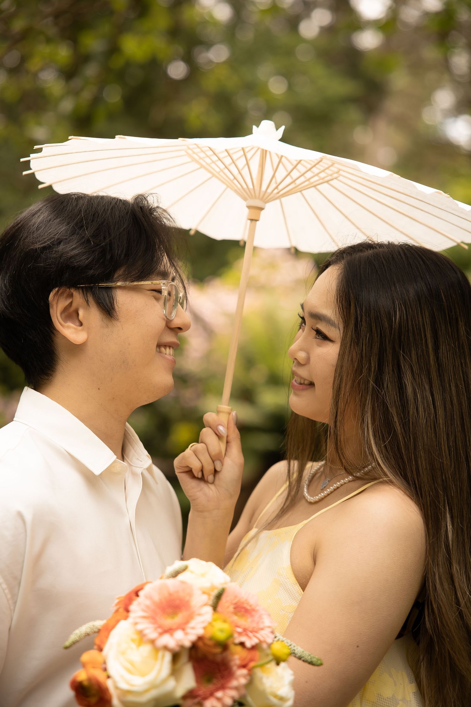 A couple shares a tender moment under a white parasol with soft bokeh lighting in the background.