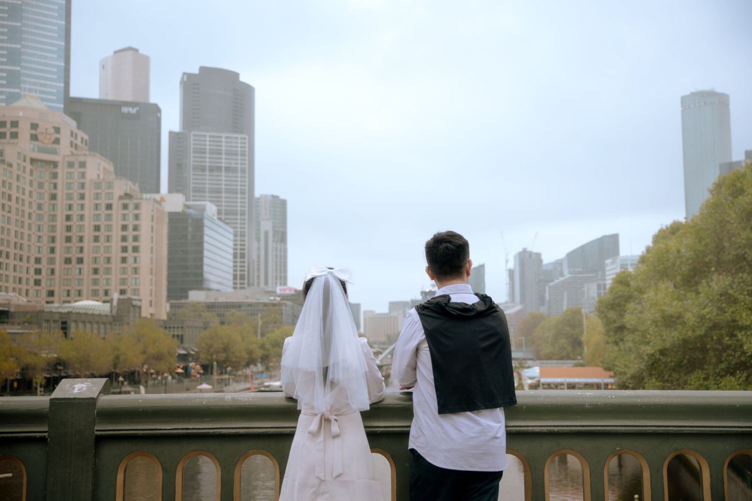 A couple in wedding attire gazes at the Chicago skyline from a bridge overlook.