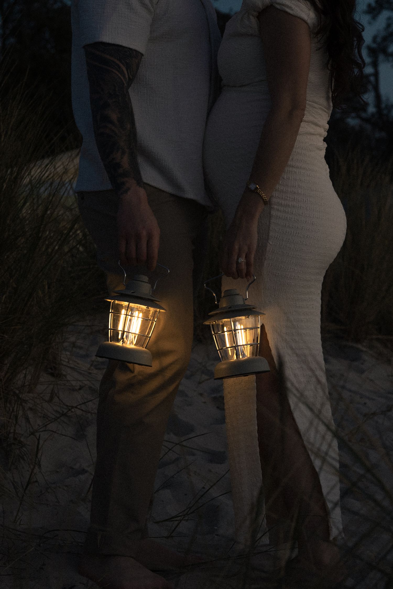 A couple walks together at dusk carrying glowing gold lanterns in their hands.