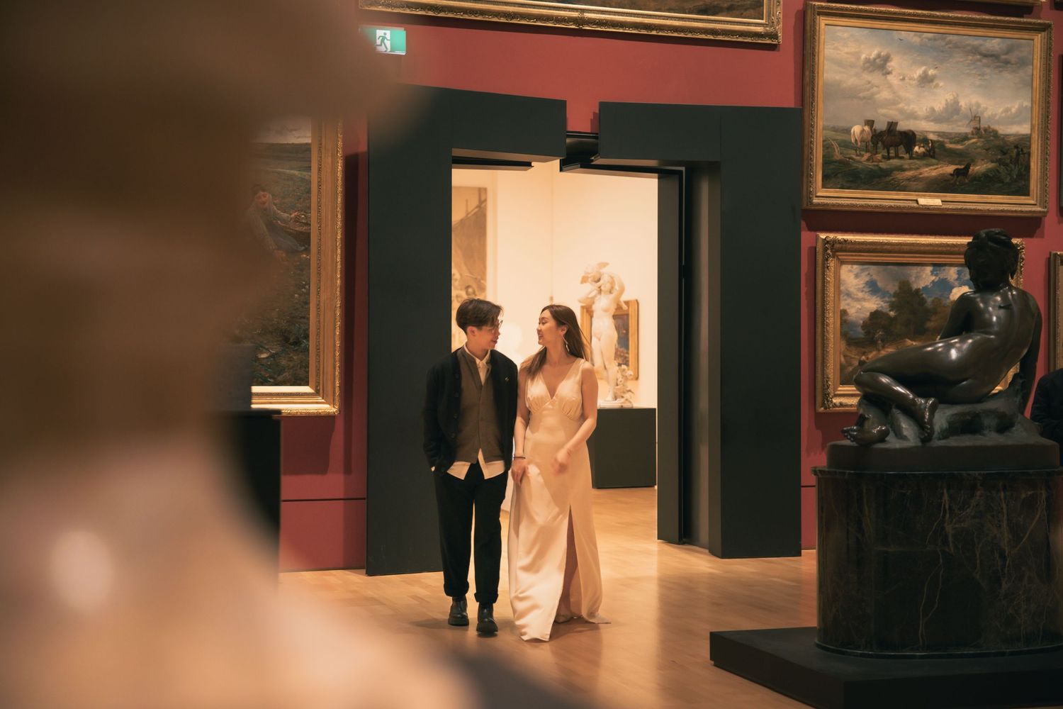 An elegant art gallery interior with paintings displayed on deep red walls.