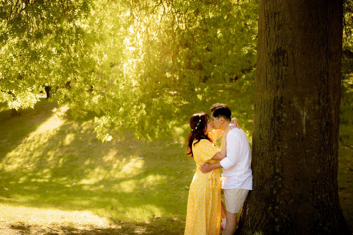 Romantic couple sharing an intimate moment under a sunlit tree in a dreamy natural setting.