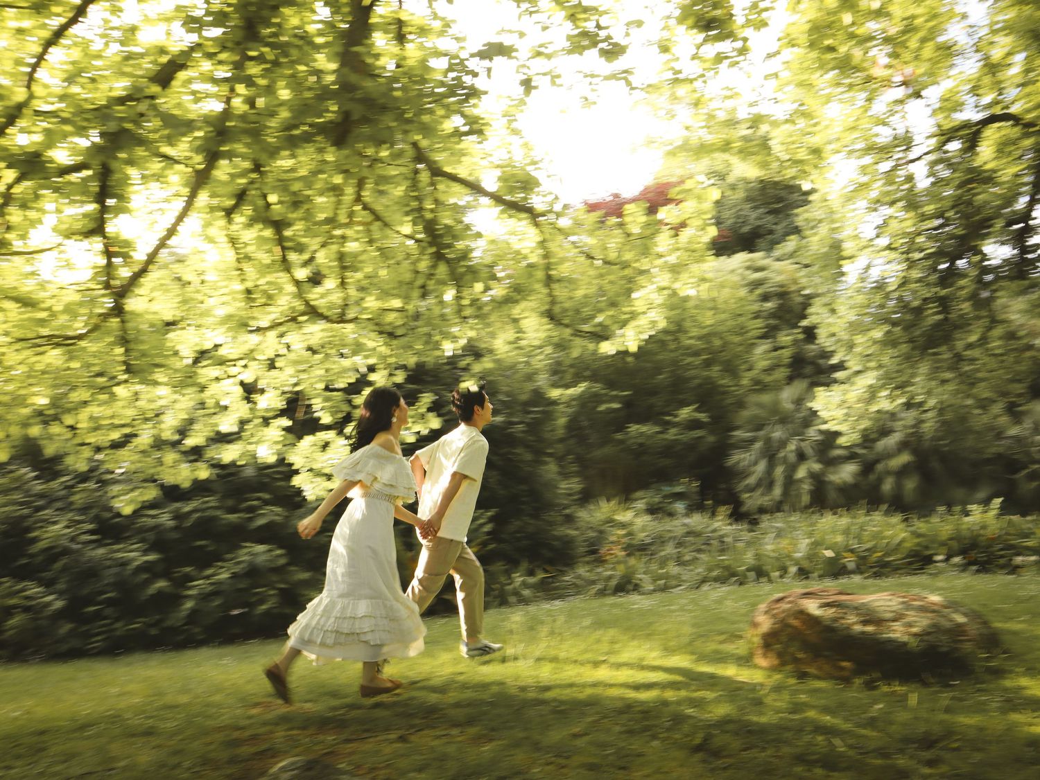 A couple dances gracefully in a sunlit garden with golden light filtering through green trees and foliage.