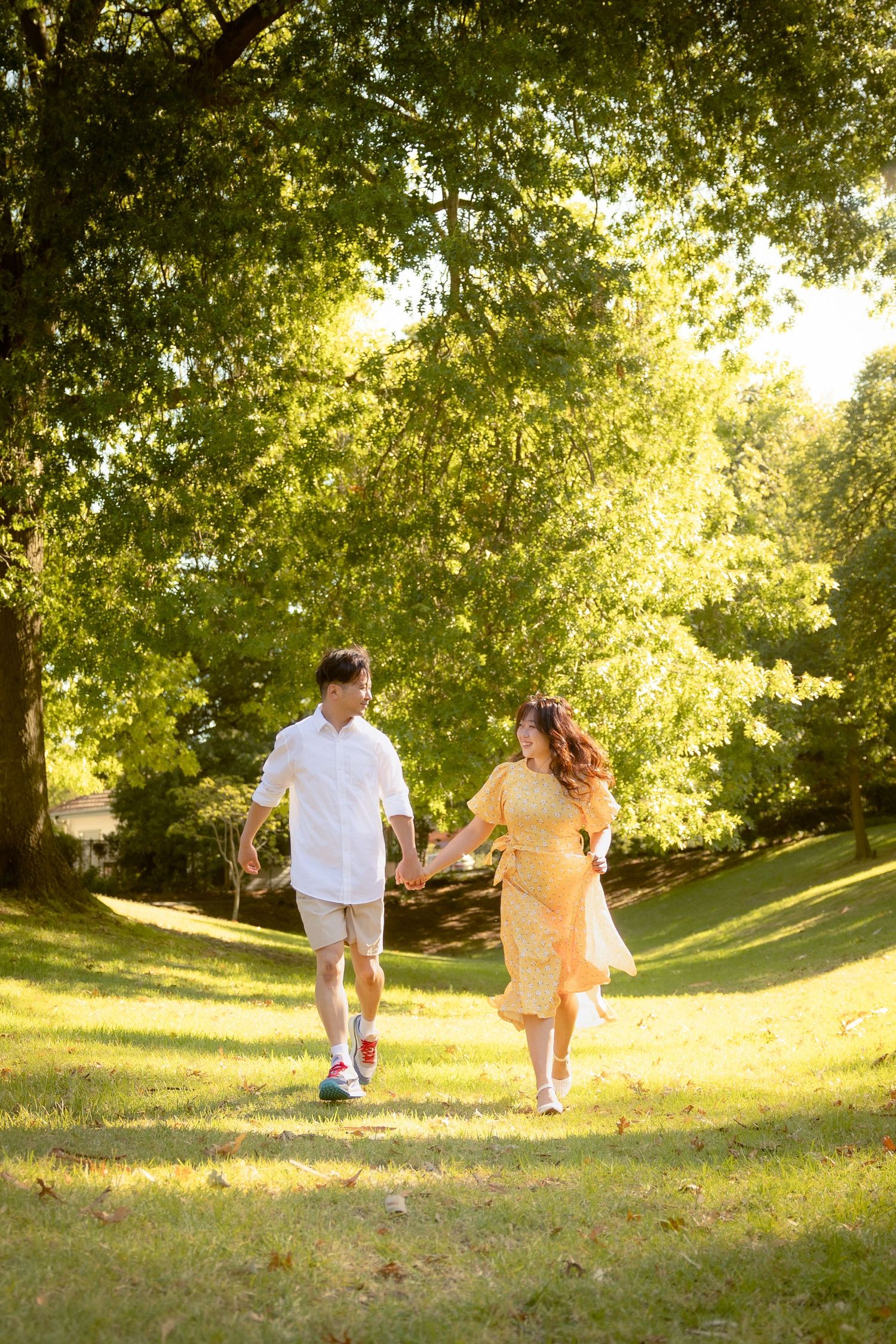 A couple holds hands while walking together through a sunlit park on a warm summer evening.