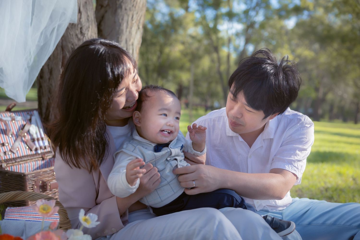 Happy family enjoying a picnic together outdoors on a sunny day in a grassy park setting.