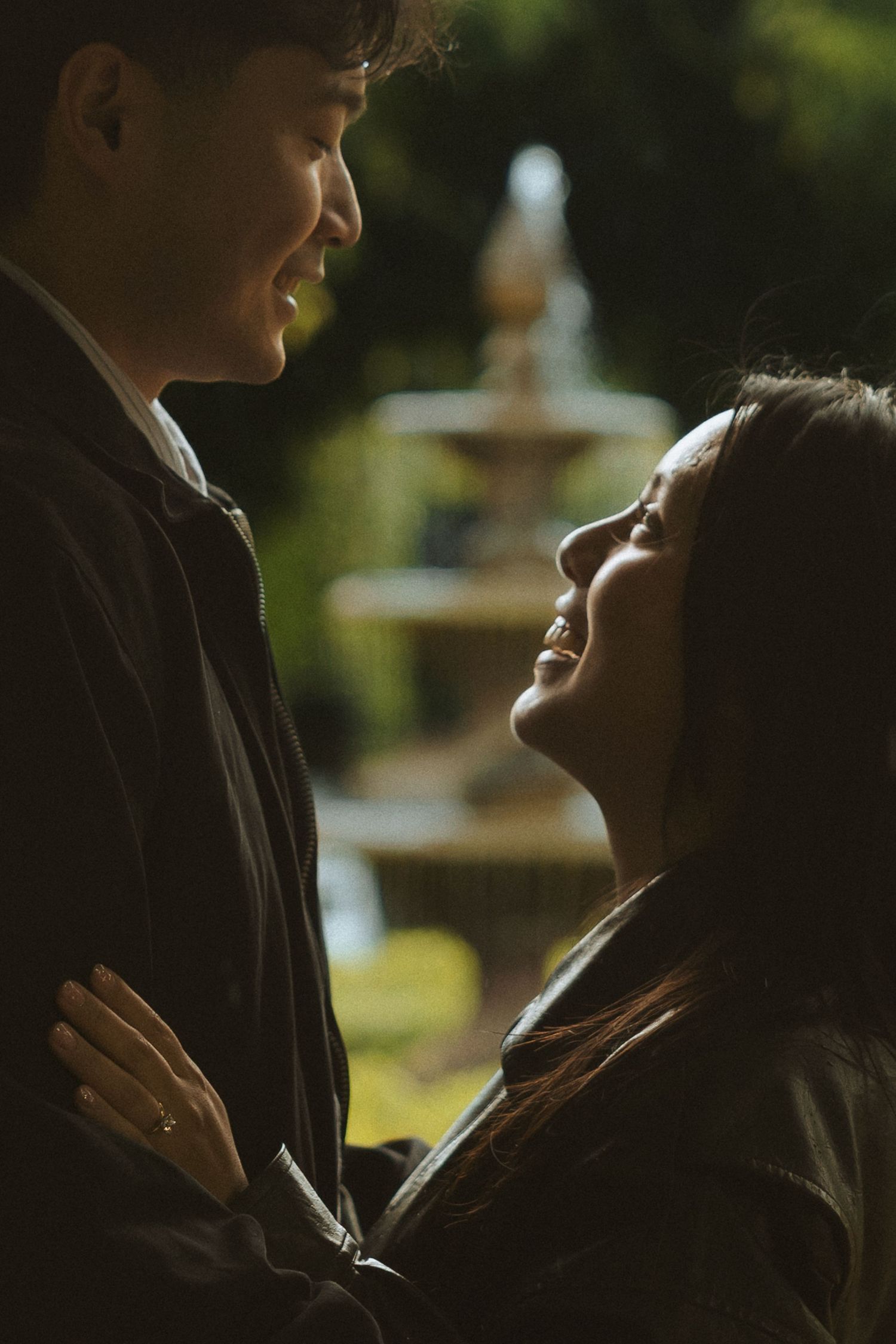 A romantic couple shares an intimate moment in front of a garden fountain during golden hour lighting.