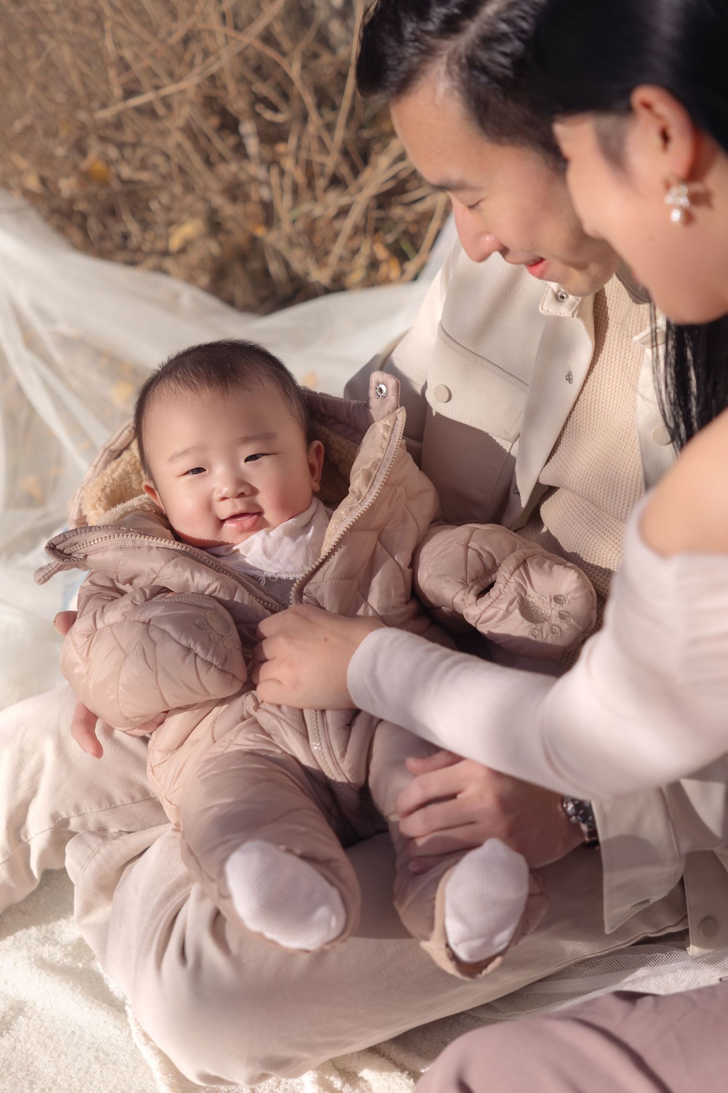 A tender photo series in soft beige tones showing loving moments with an infant on a light-colored blanket.