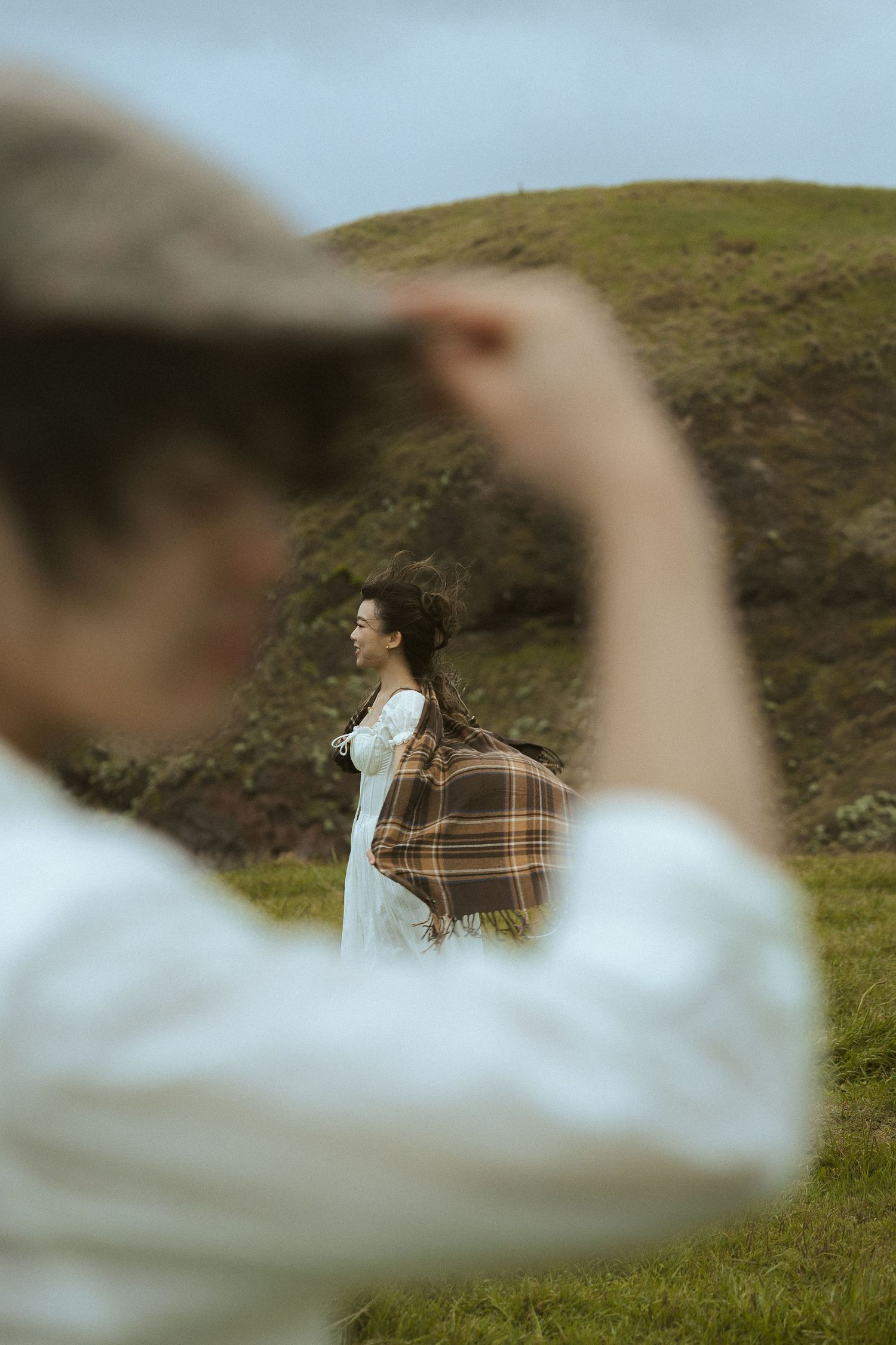 Couple standing together in green rolling hills during golden hour, with focus shifting between foreground and background.