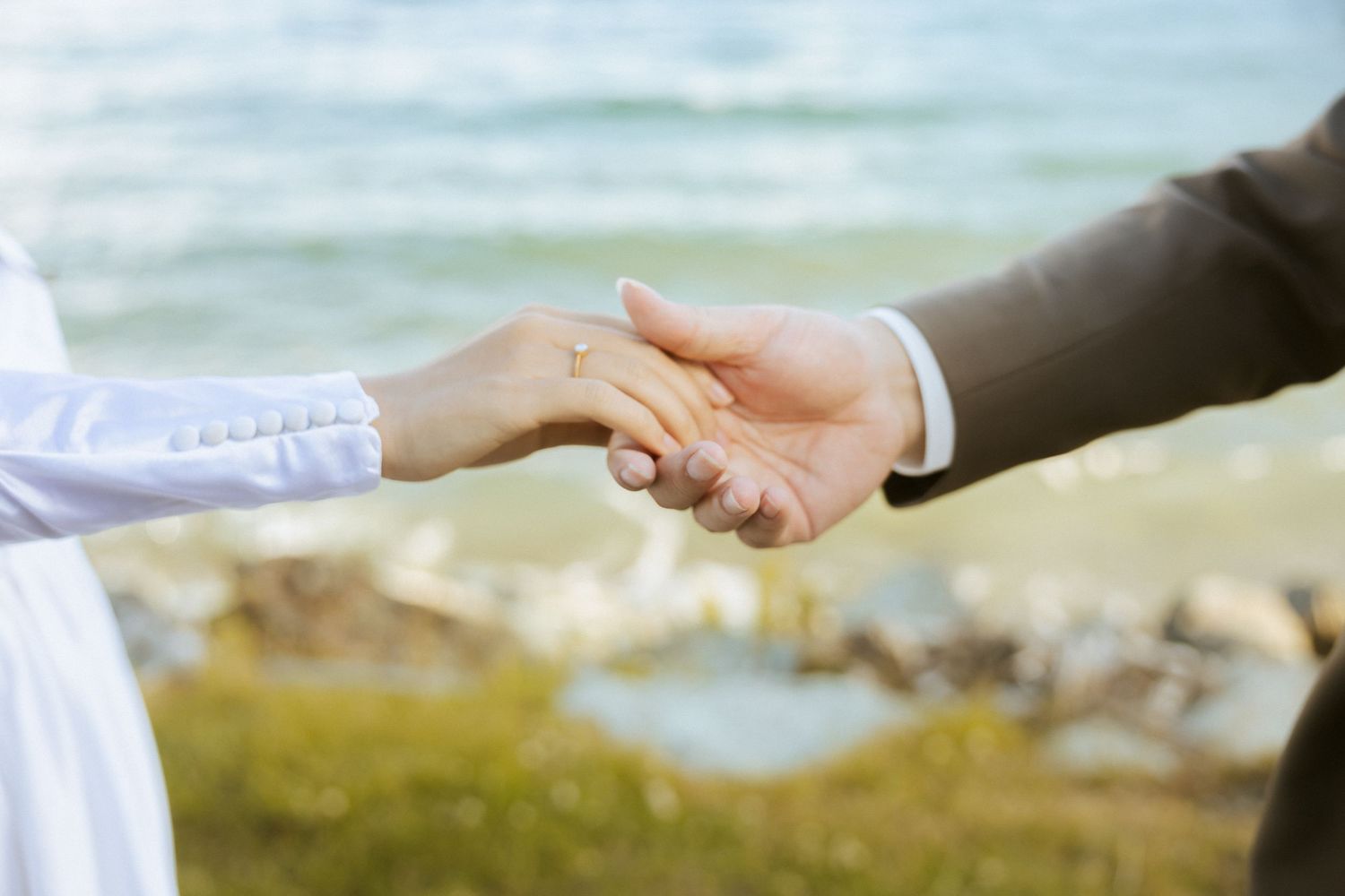 Two hands reaching toward each other against a blurred outdoor background in warm sunlight.