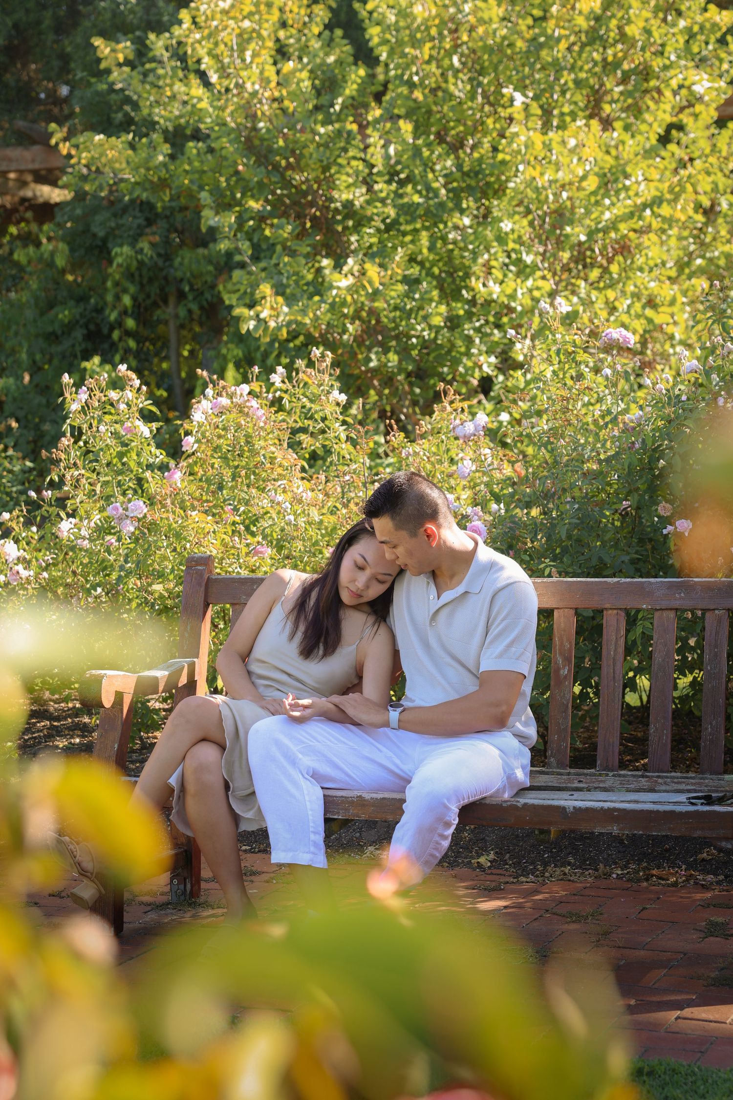 Tender moment shared on a wooden bench surrounded by blooming garden flora.