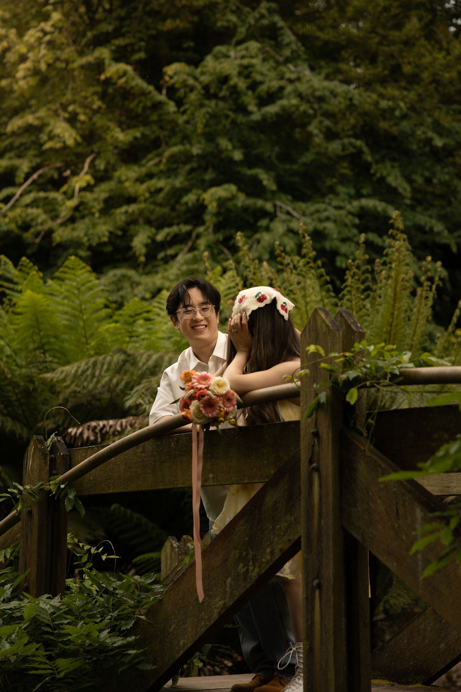 A playful moment captured on a rustic wooden bridge surrounded by green ferns and forest foliage.