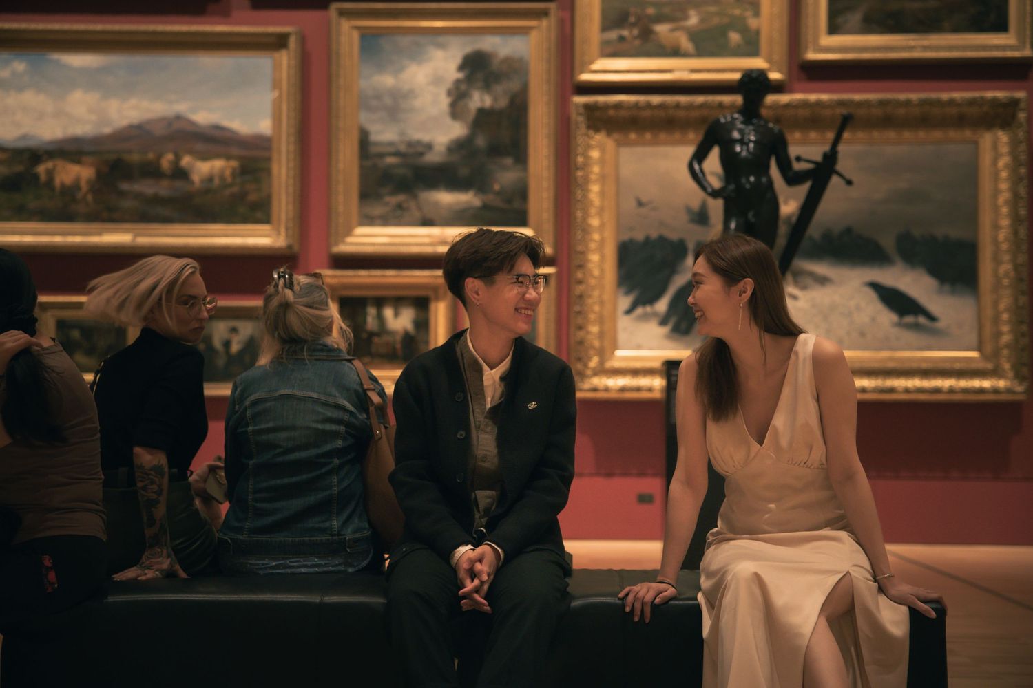 Couples share romantic moments in an art gallery with classical paintings on burgundy walls.