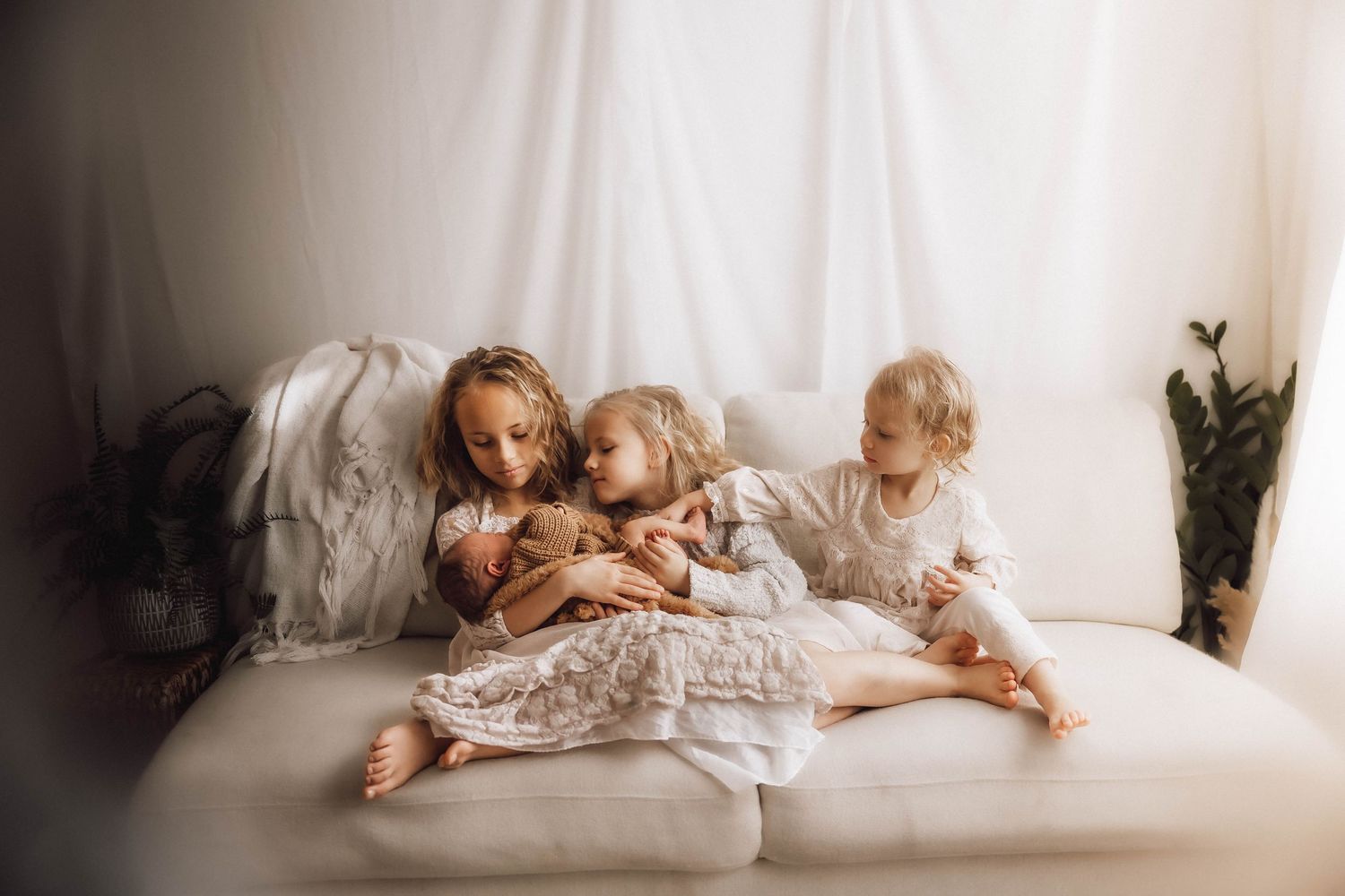 A dreamy family scene with small children cuddling together on white bedding in natural light.