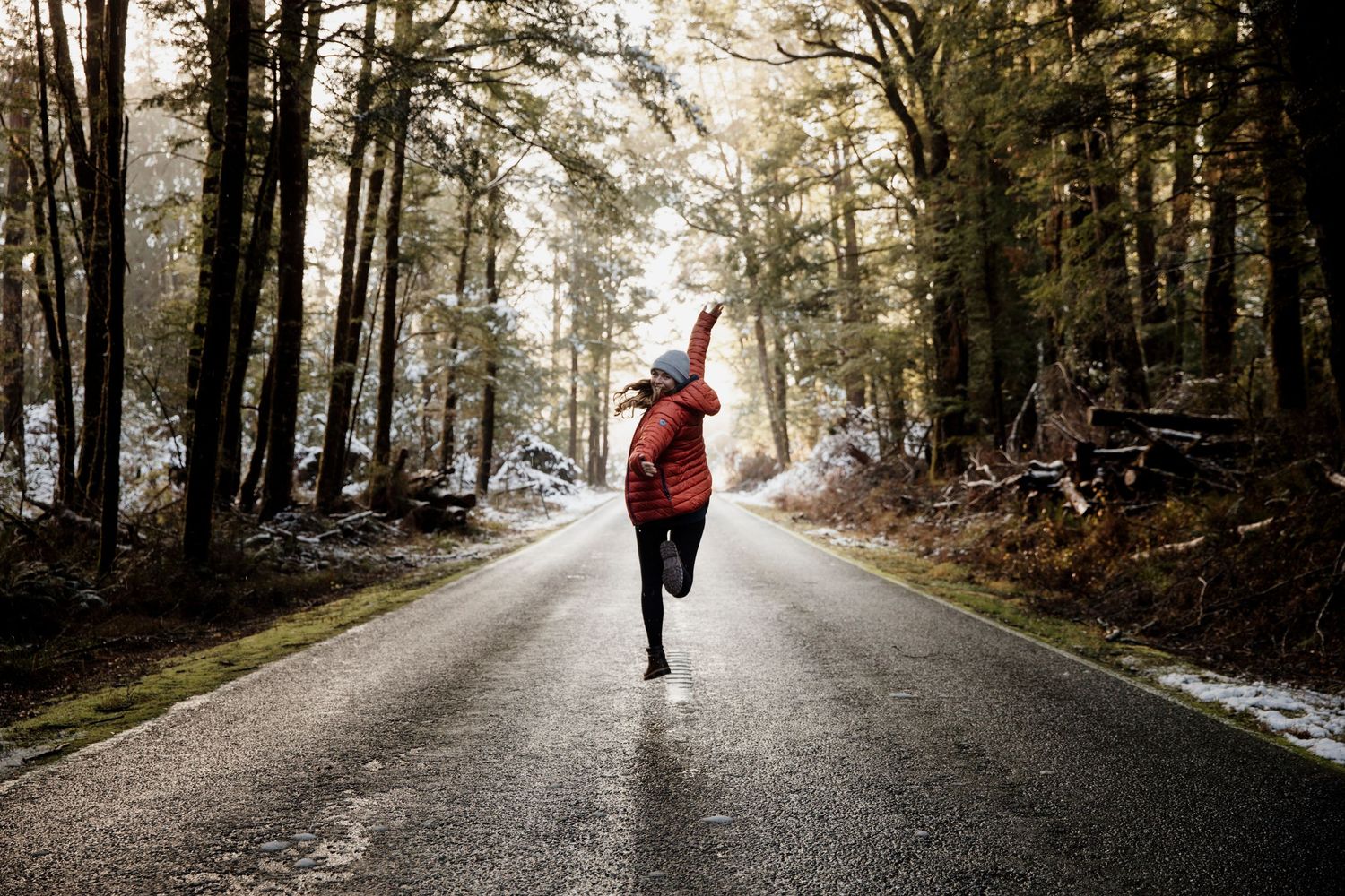 Person in red jacket jumping on snowy forest road in winter woods.