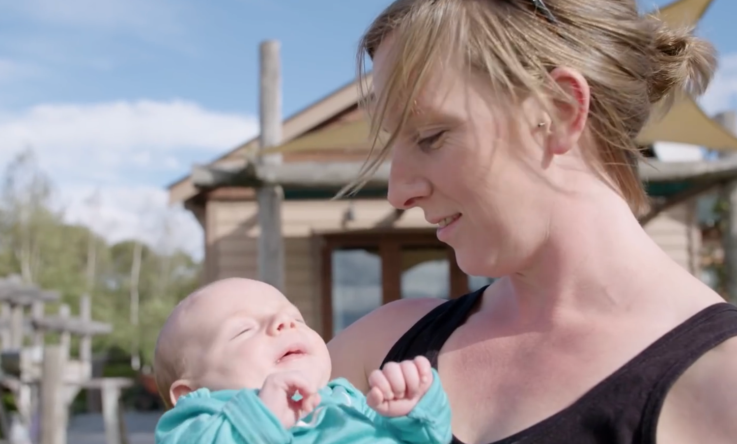 A woman tenderly holds a sleeping newborn baby outdoors after him almost dying at birth due to a lack of funding and support in Wanaka.