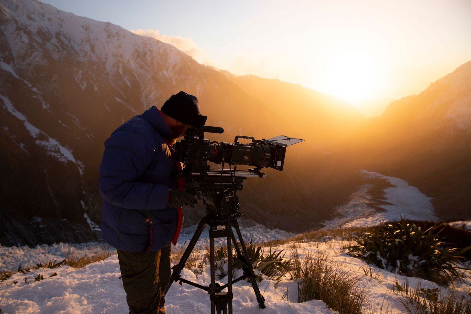 Videographer filming snowy mountain valley landscape at golden sunset hour for BBC's Frozen Planet 2 series.
