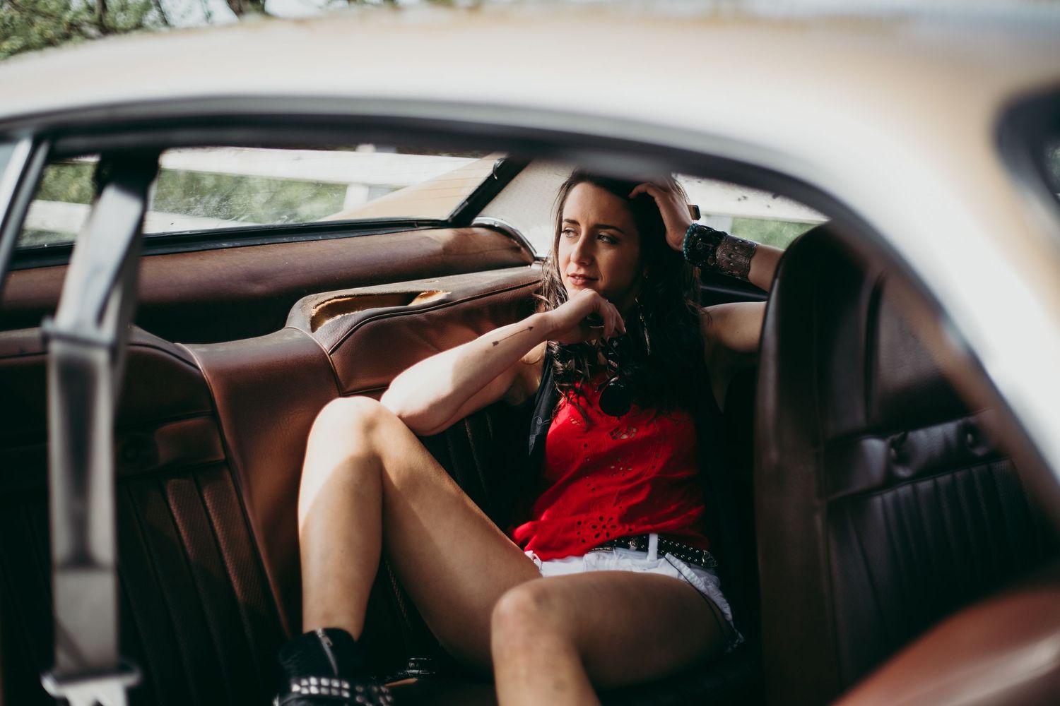 Kaylee Bell in red top sitting in the back seat of a vintage classic car interior for her music video.