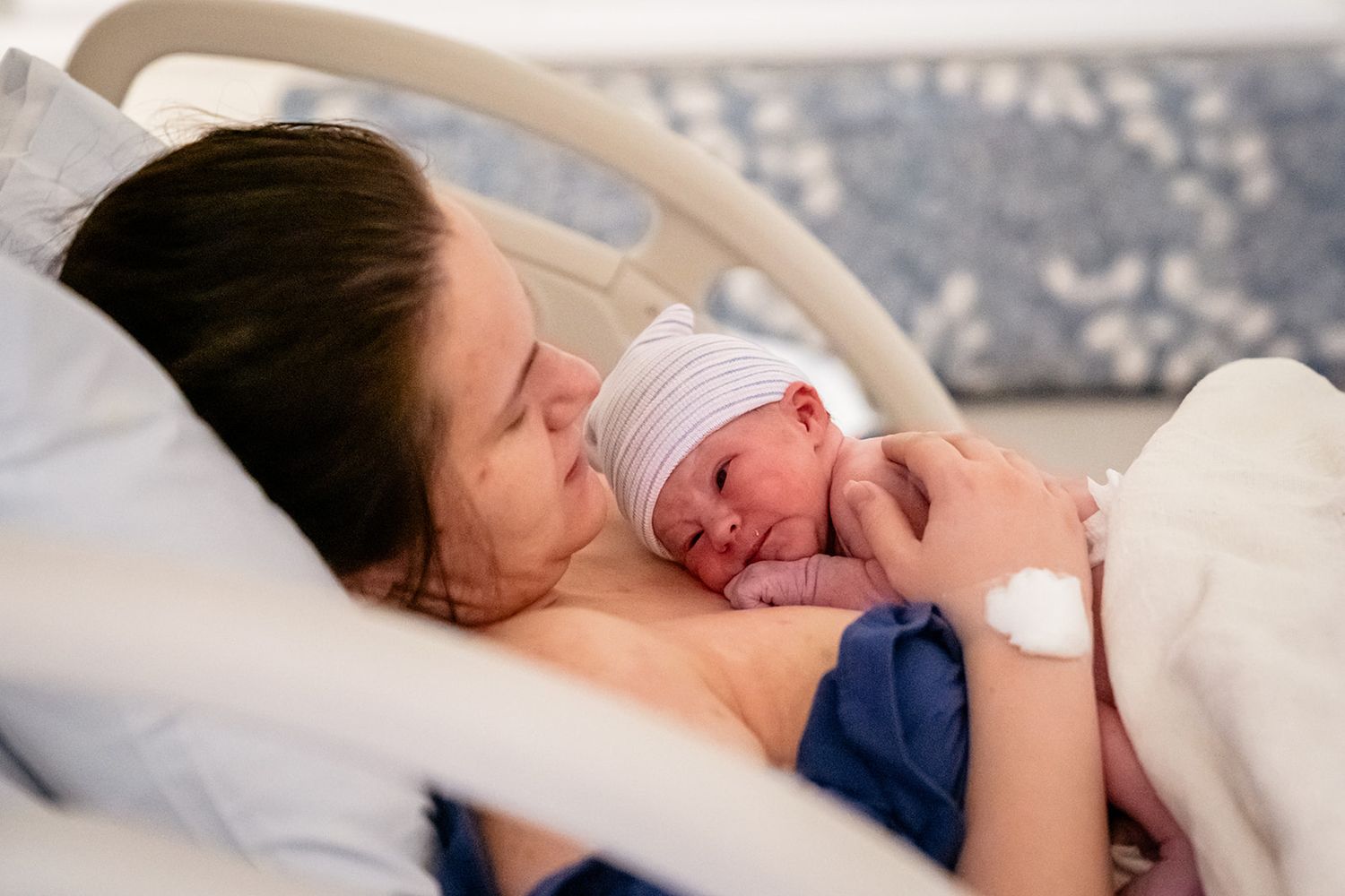 New mother lying in hospital bed holding newborn baby skin-to-skin after delivery.
