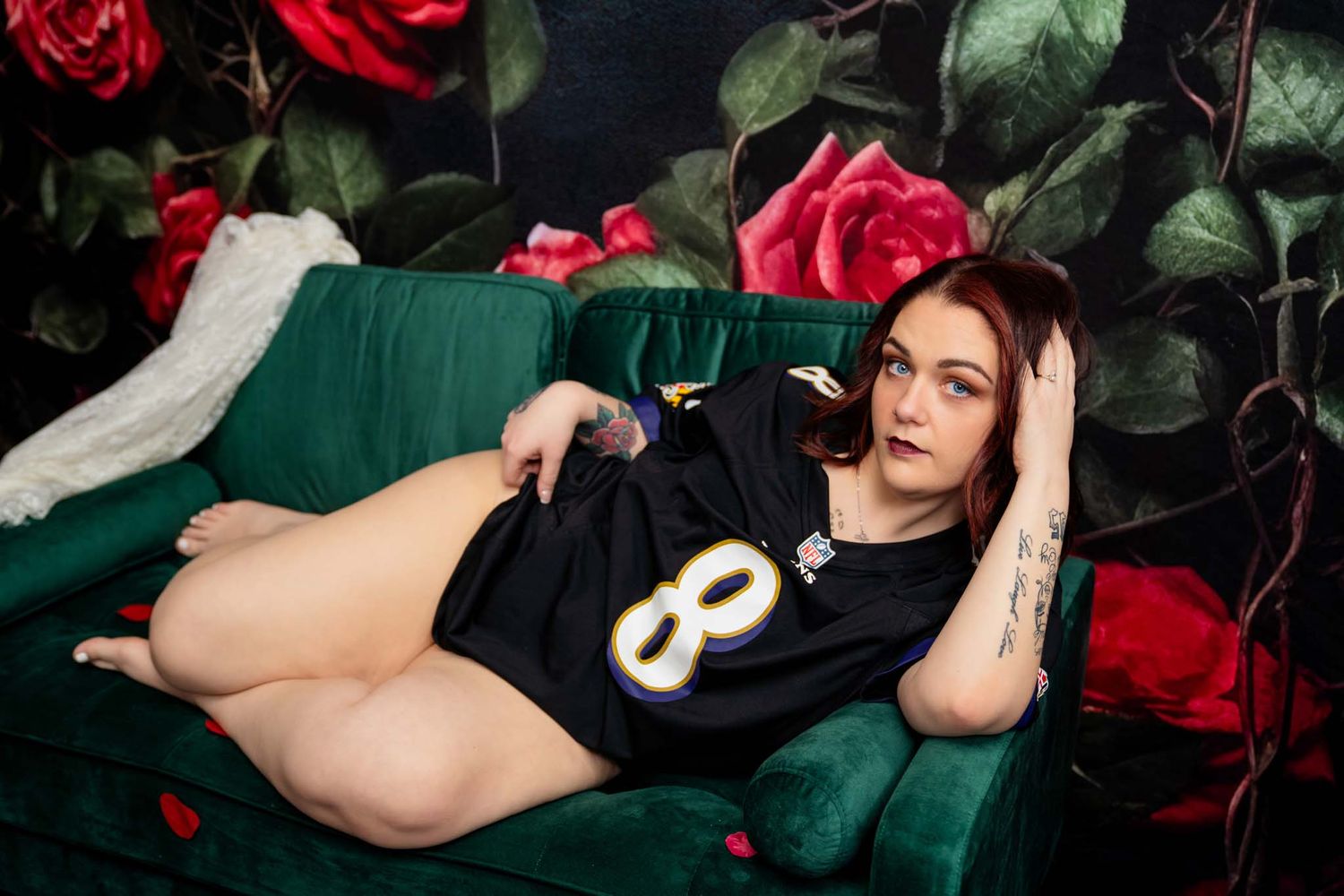 Woman in football jersey reclining on green velvet sofa with floral backdrop.