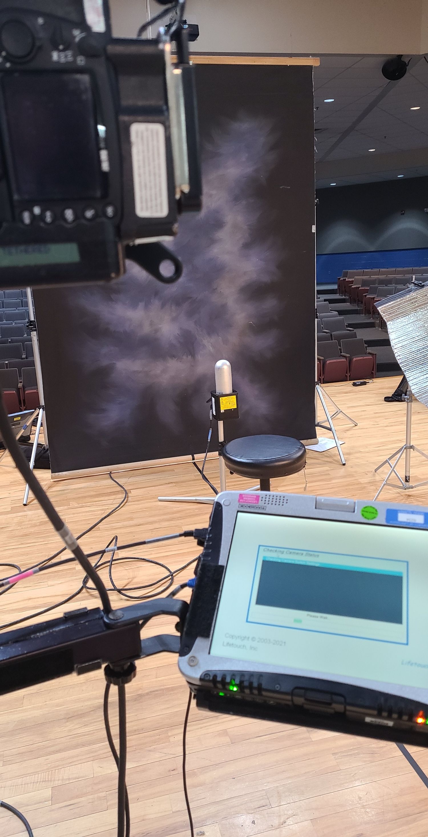 Professional photo studio setup with laptop, camera, and dark cloudy backdrop in an auditorium setting.