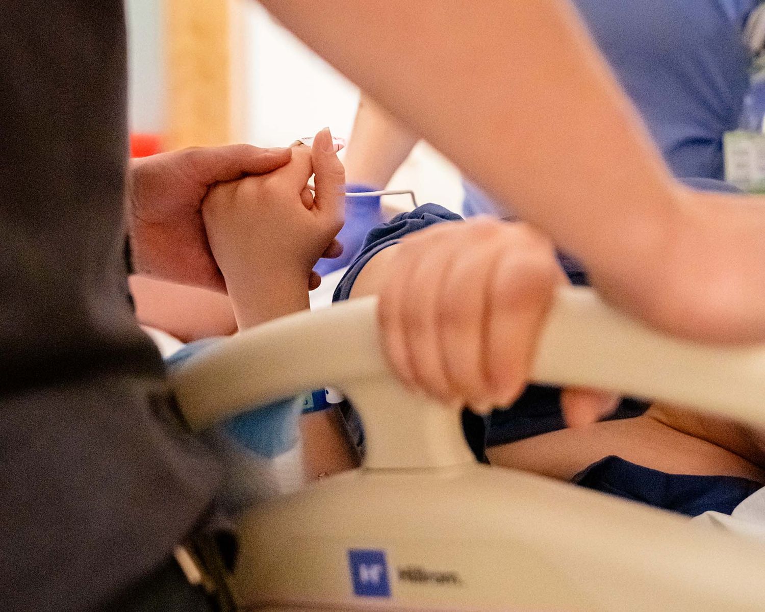 Medical professional holds patient's hand during a clinical procedure in a healthcare facility.