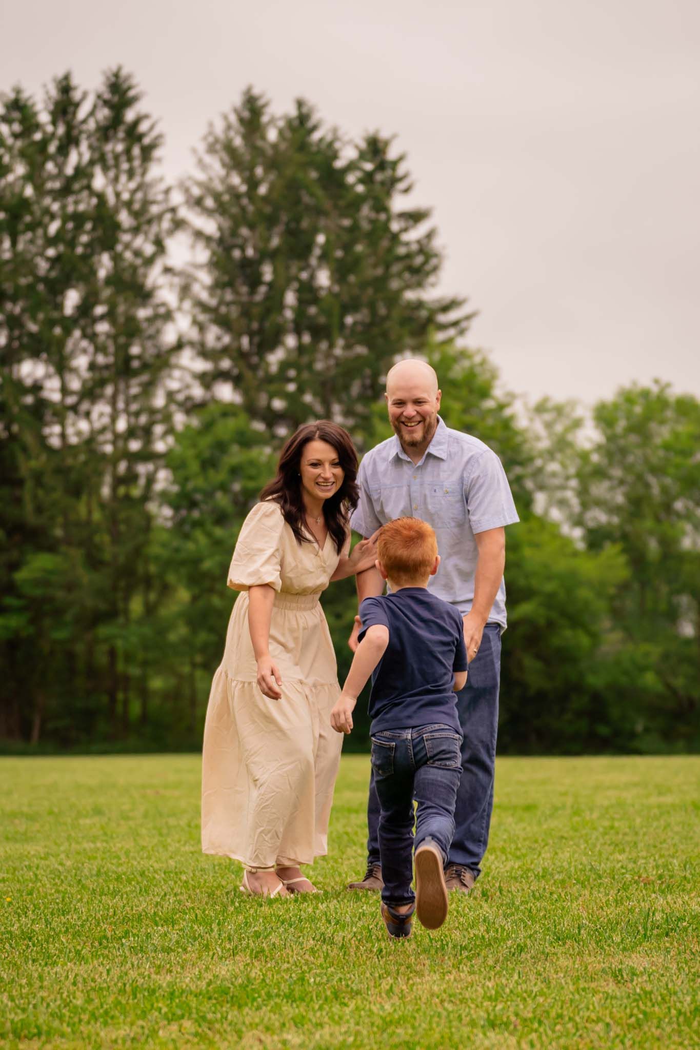 Joyful family moment as redhead boy runs toward laughing parents in field.