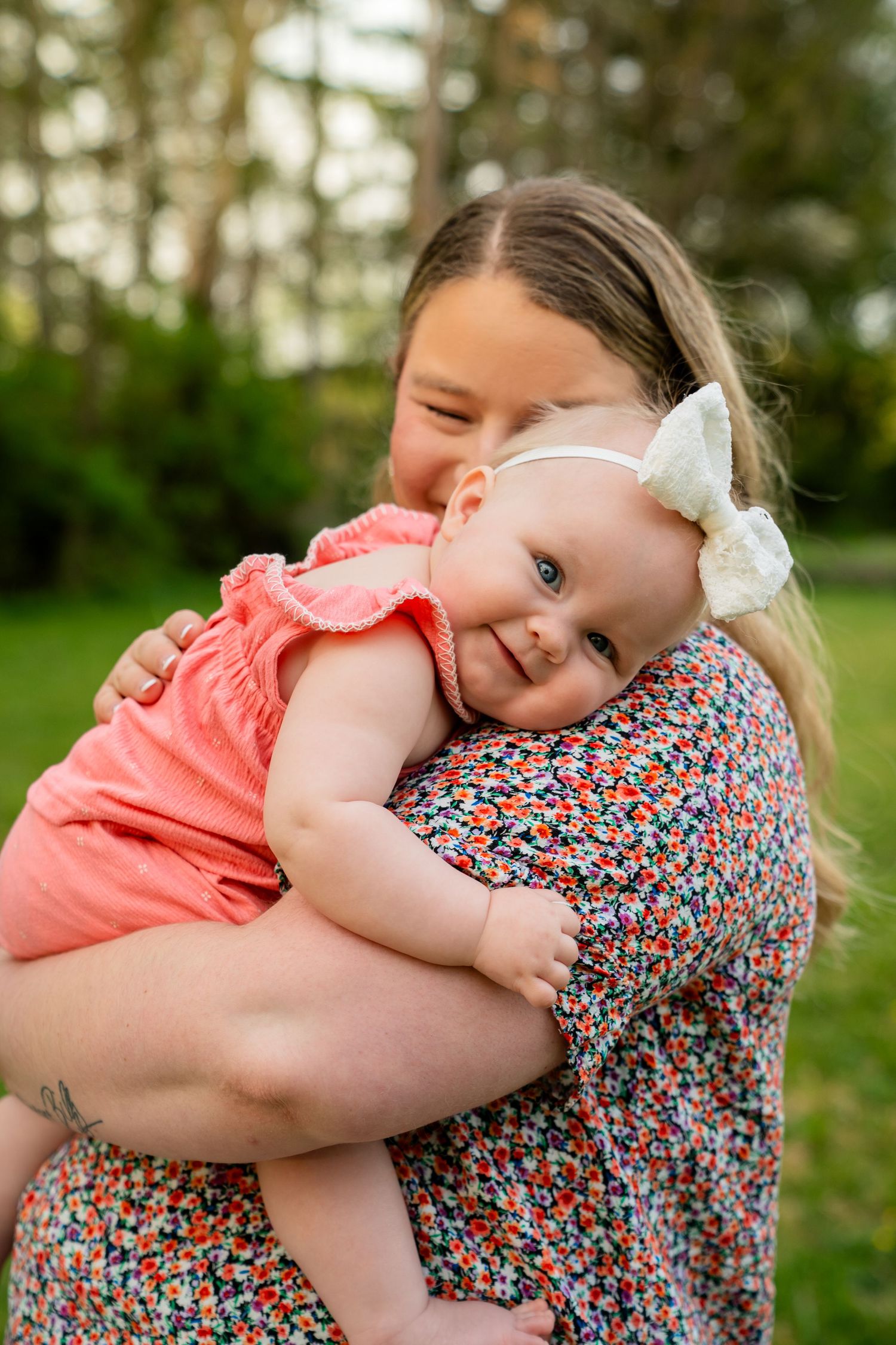 Young girl holding smiling baby in pink romper during outdoor portrait session.