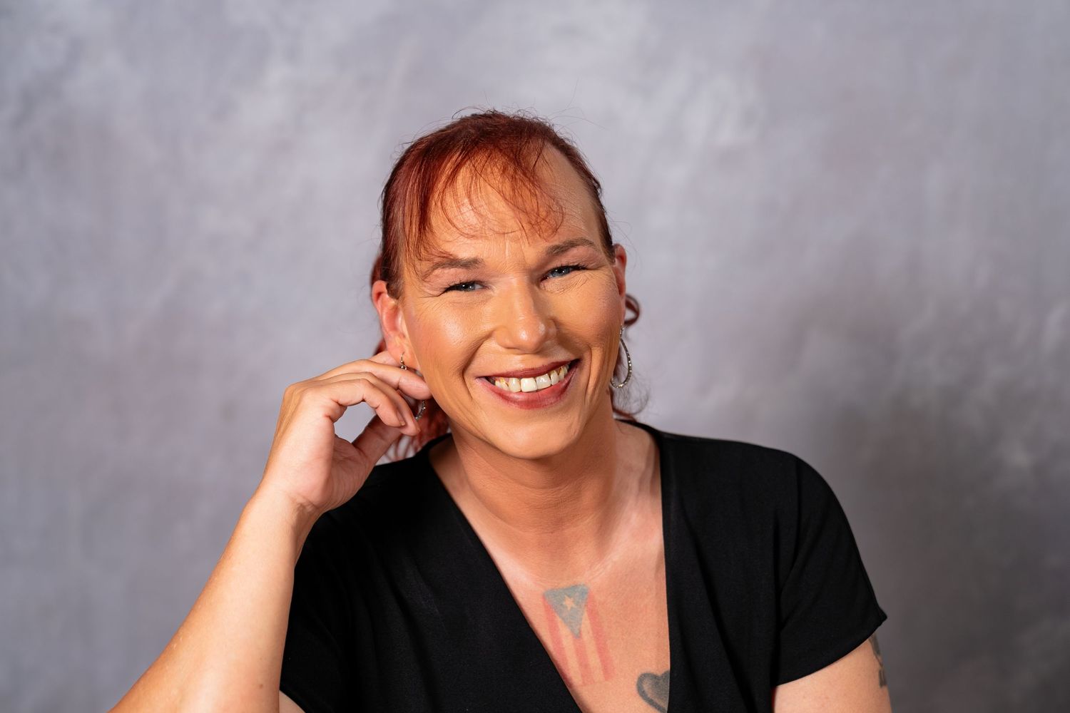 Joyful redhead woman laughing with hand near face in black top against gray studio background.