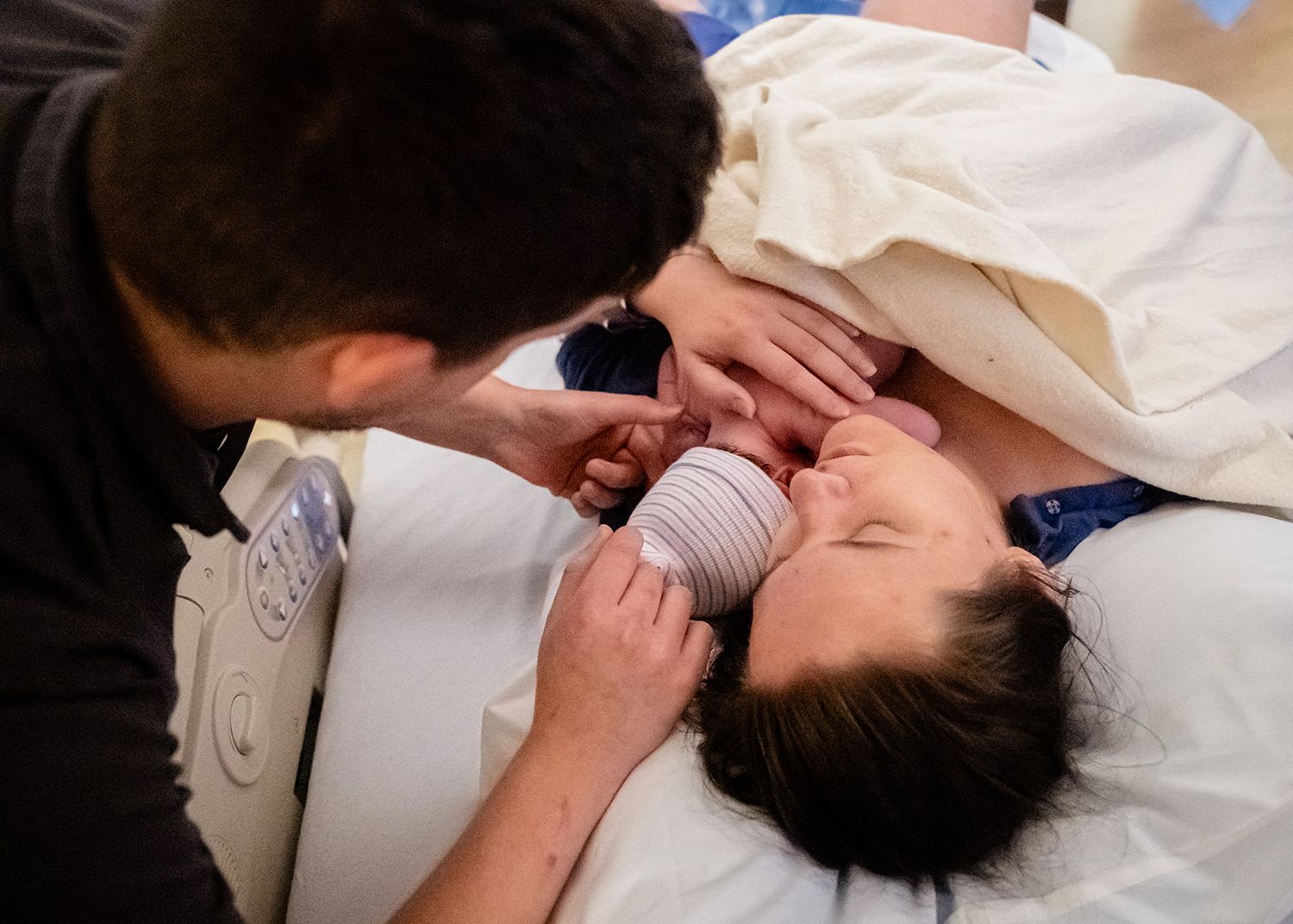 Emotional parents sharing a tender moment with their newborn baby in a hospital delivery room.