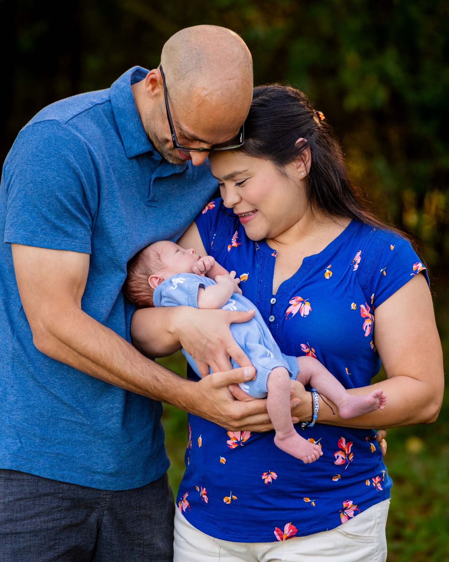 Couple in matching blue outfits tenderly holding their newborn baby outdoors in nature.