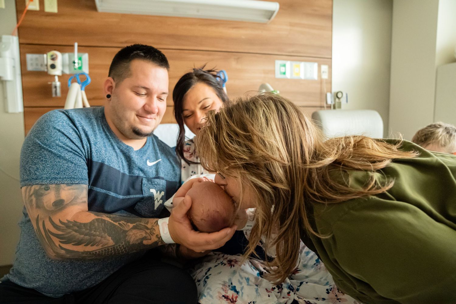 Family gathered around newborn baby in hospital room, parents and grandmother sharing a tender moment.