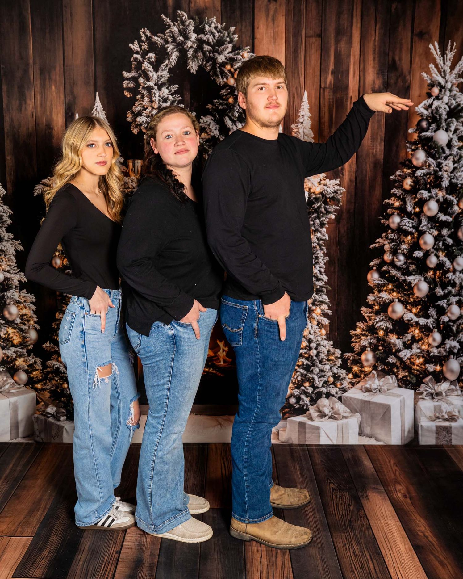Three teenagers posing confidently in front of decorated Christmas trees in a professional studio setting.