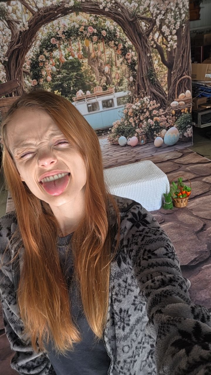 Woman with red hair laughing joyfully in front of a floral arch Easter-themed photo backdrop.