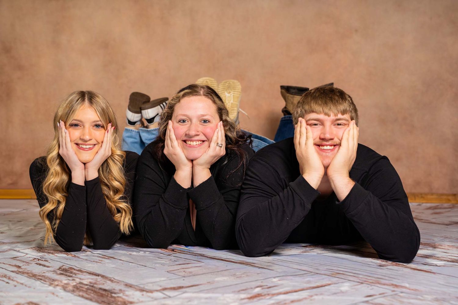 Three people lying on the floor smiling with chins resting on hands in a fun studio photo session.