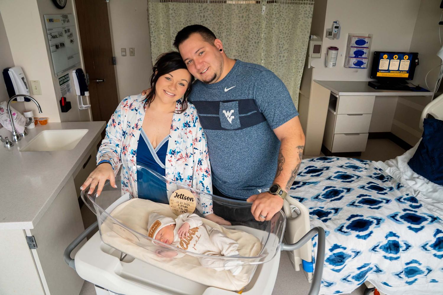 New parents smile proudly beside their newborn in a hospital bassinet after delivery.