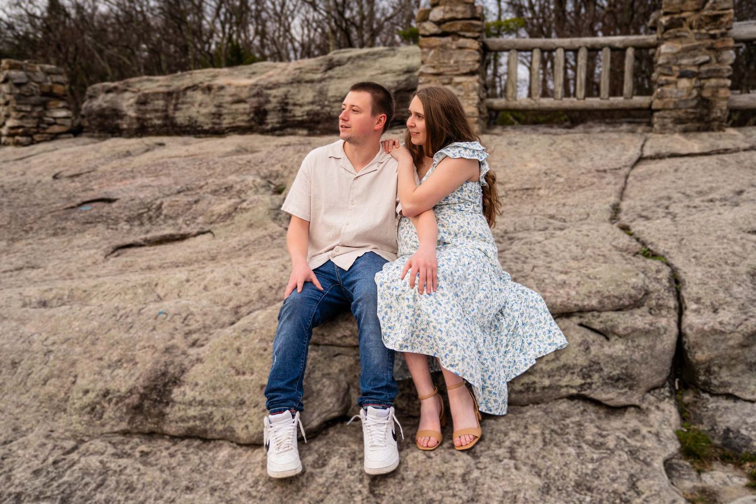 Young expecting couple sits together on rocky surface during outdoor maternity photography session.