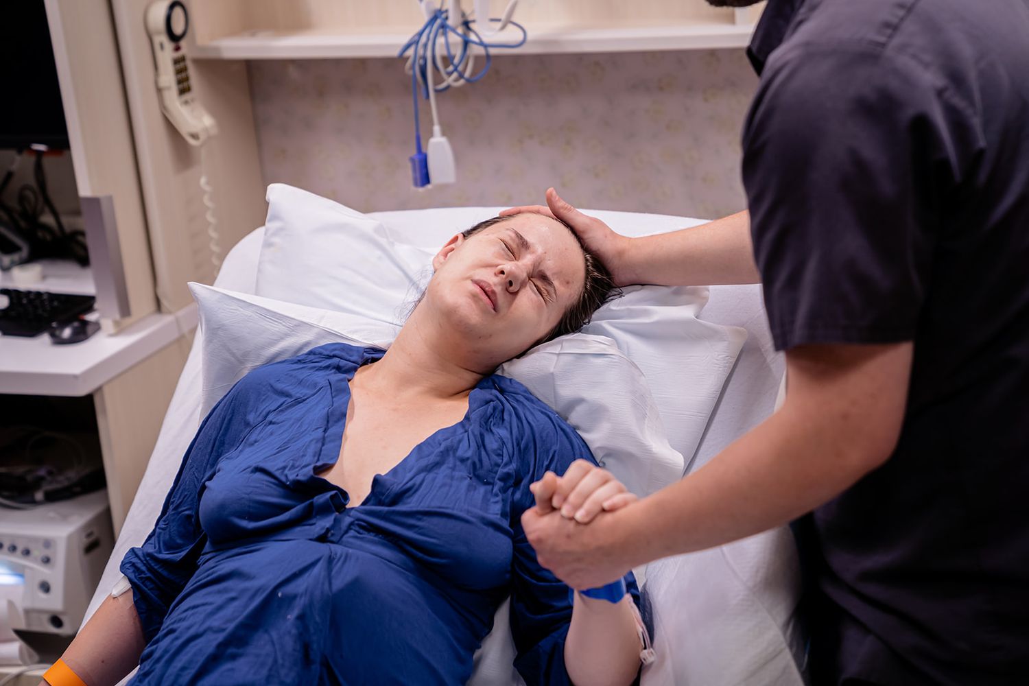 Nurse comforting laboring woman in hospital bed, holding her hand and supporting her head during contractions.