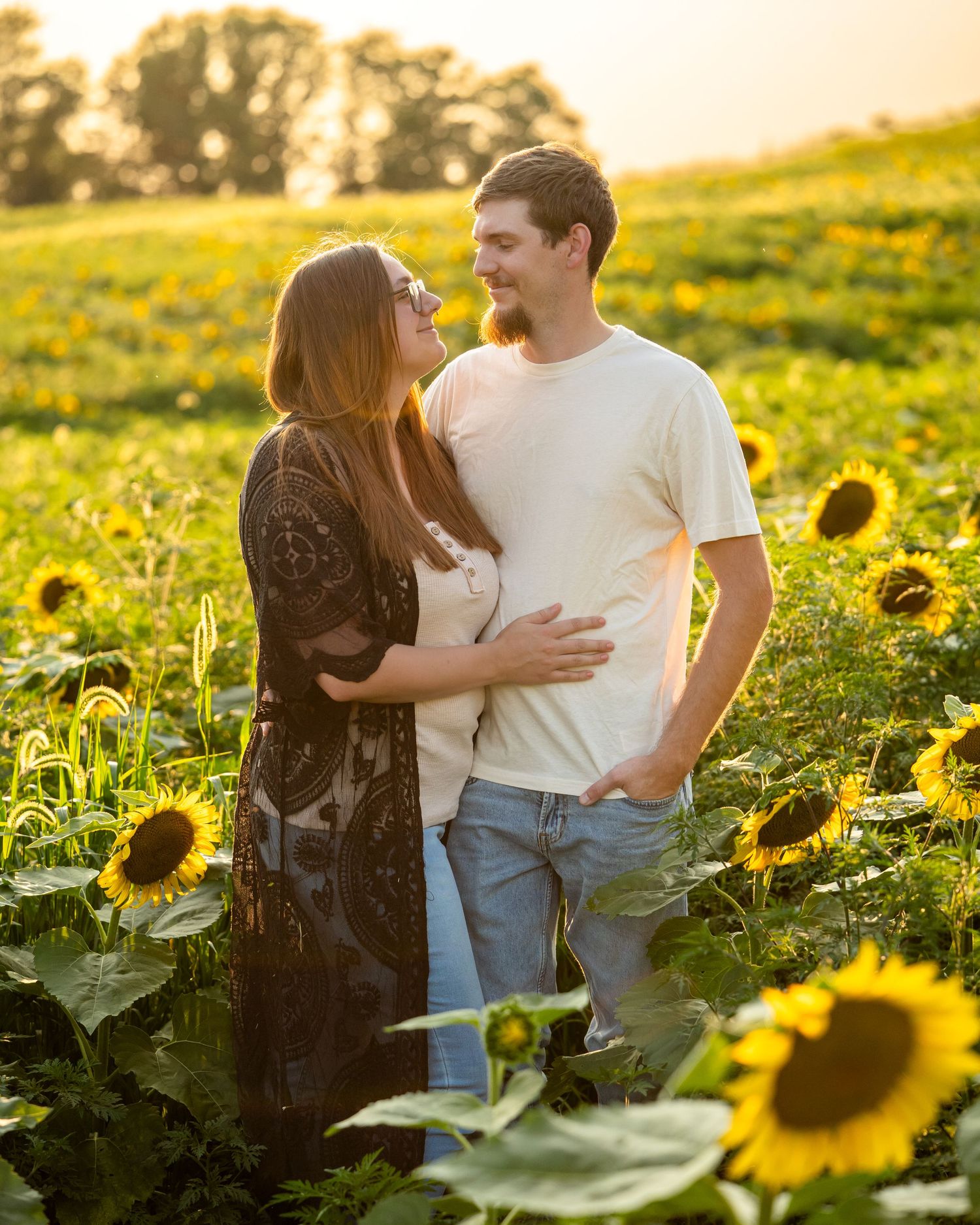 Couple embracing in a sunflower field at golden hour, sharing a romantic moment outdoors.