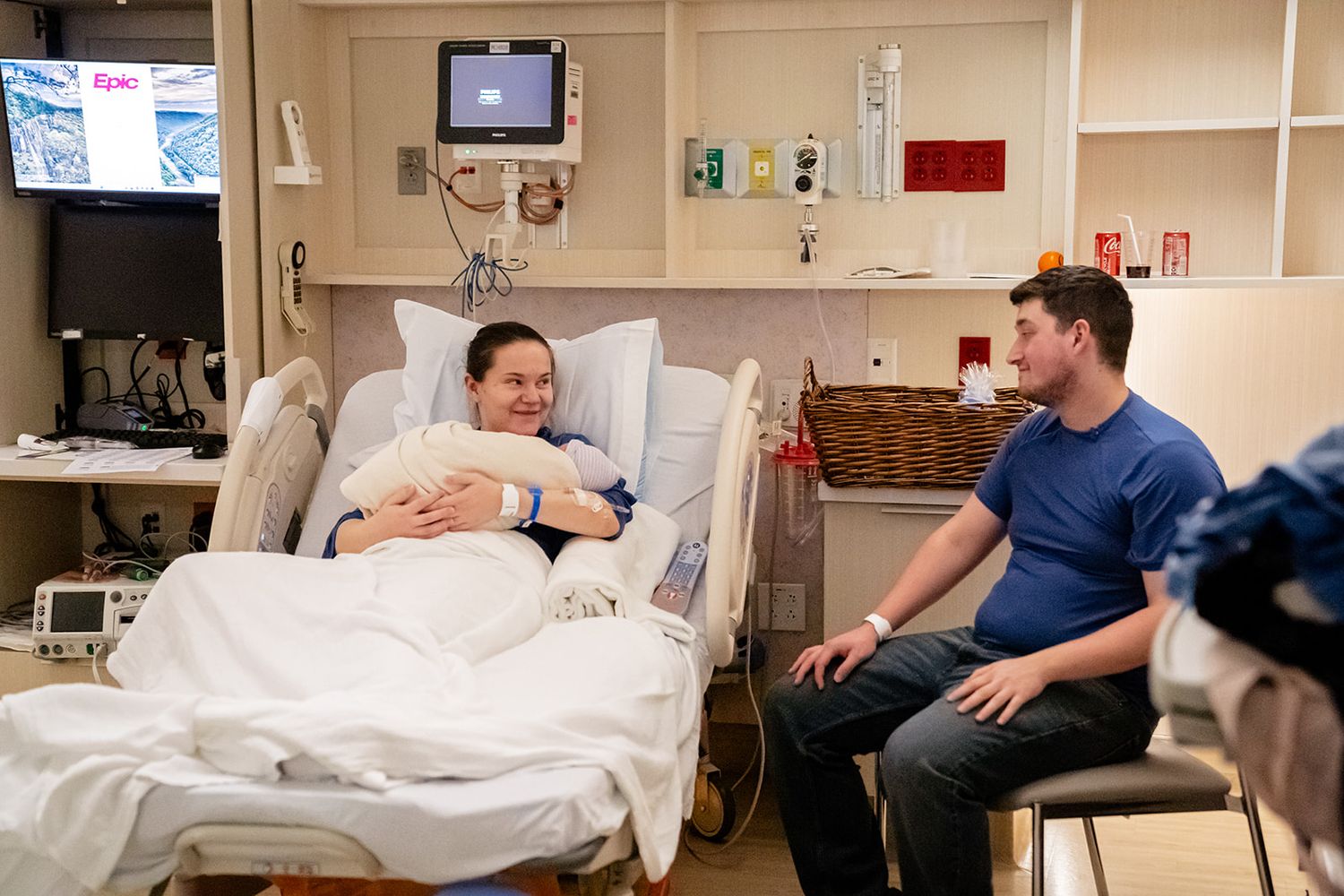 New mother resting in hospital bed smiling at father seated beside her after childbirth.