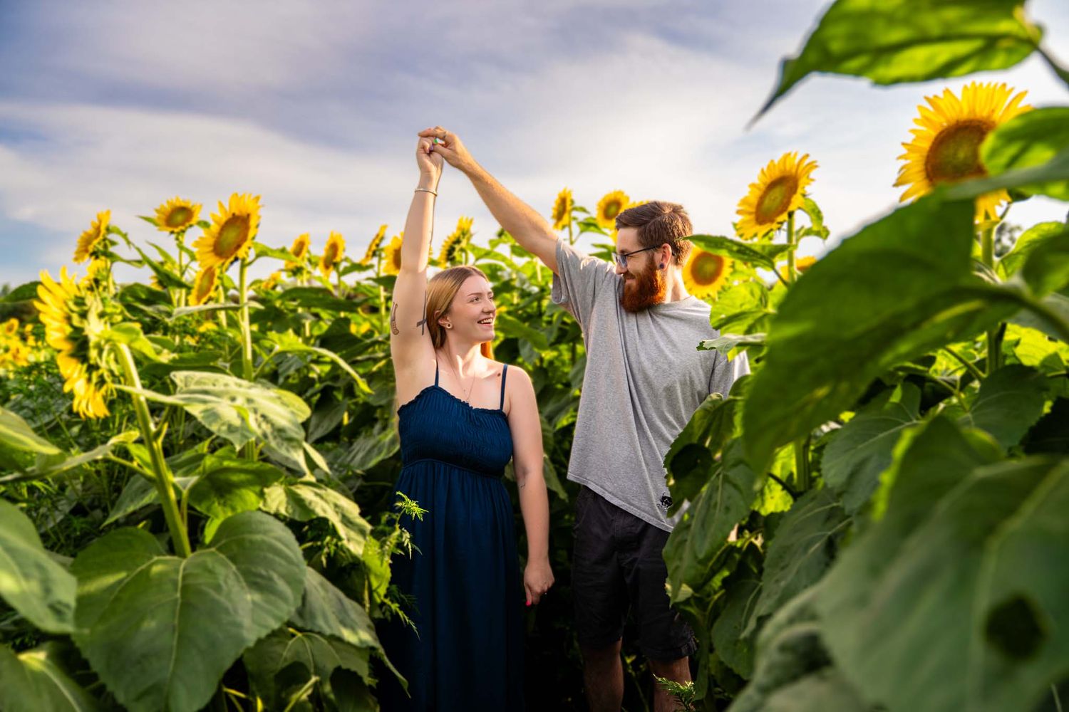 Couple dancing joyfully among tall sunflowers in a sunny field.