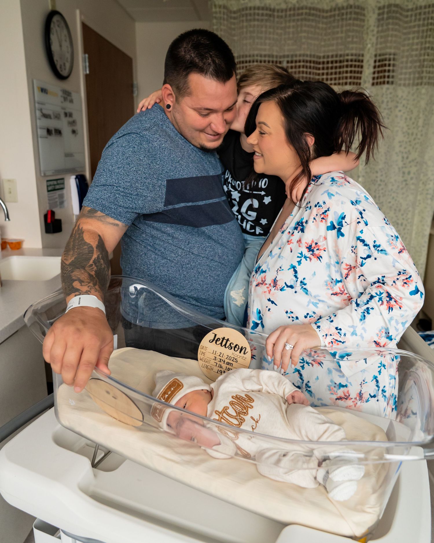 New parents and family admire newborn baby Jettson in hospital bassinet, sharing a tender moment.