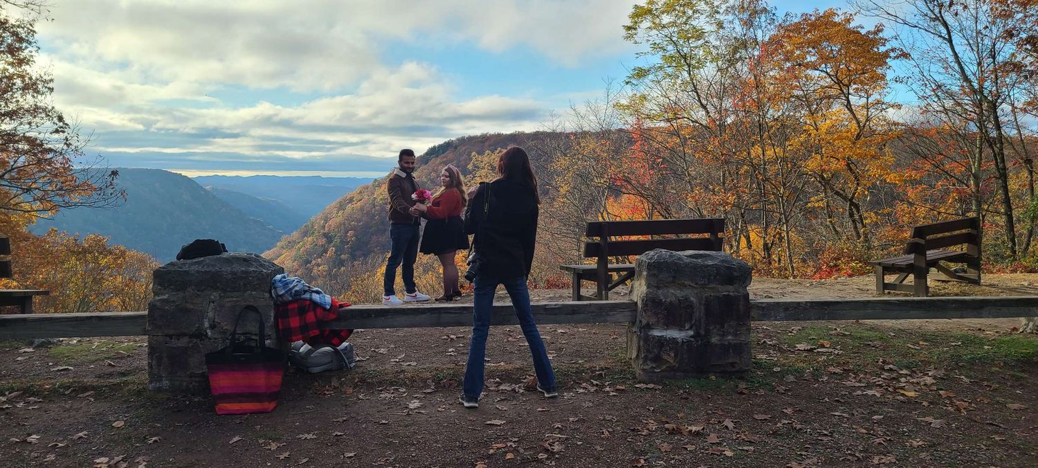 Hikers enjoying a scenic autumn overlook with colorful fall foliage and mountain valley views on a cloudy day.
