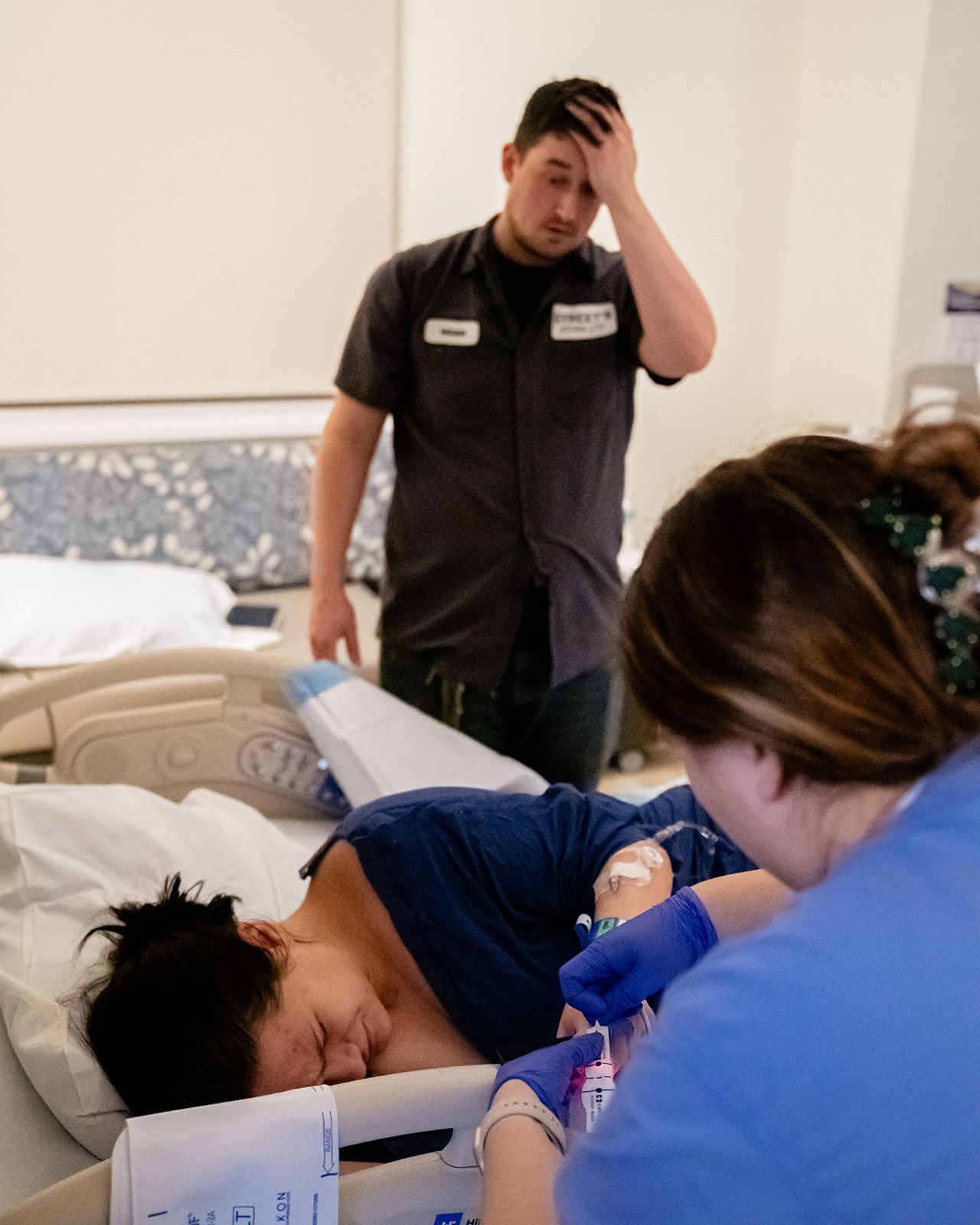 Concerned father watching nurse draw blood from laboring wife in hospital delivery room.