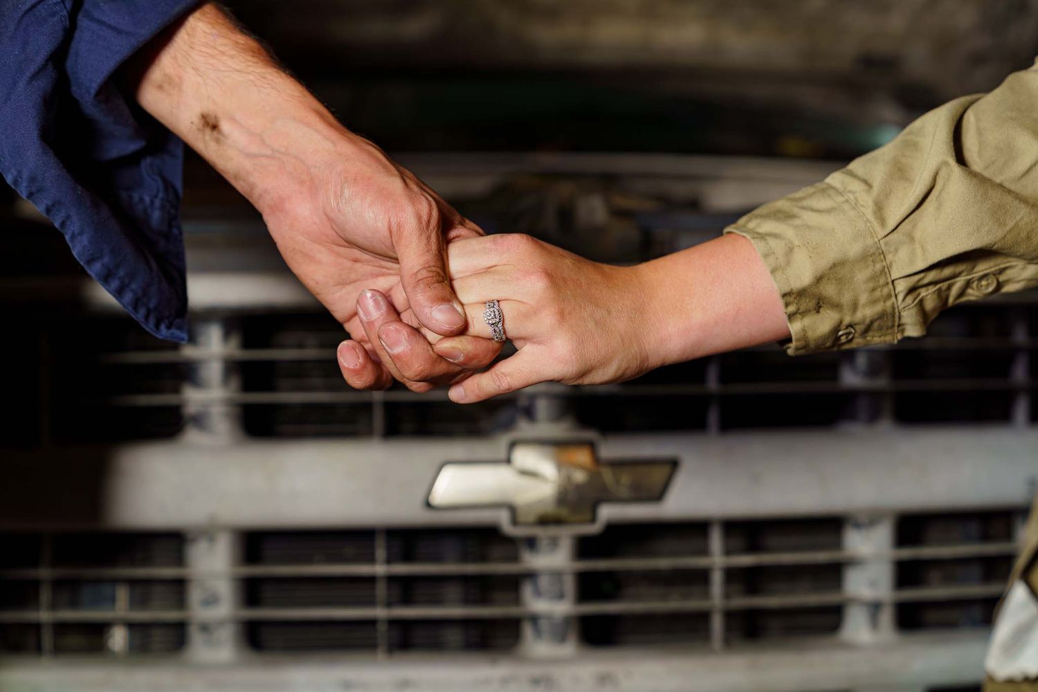 Close-up of a couple holding hands in front of a classic Chevrolet truck grille in a garage.