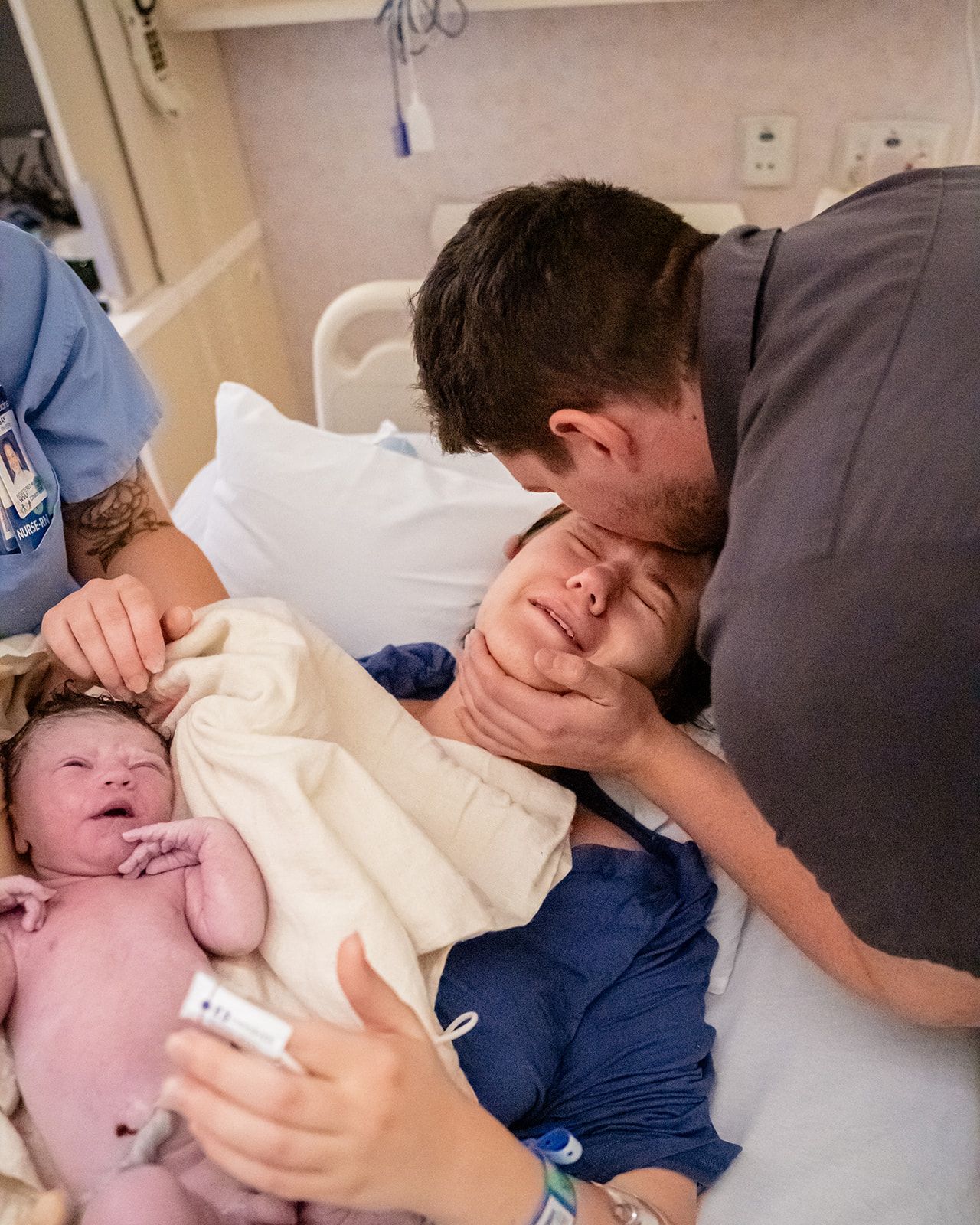New parents emotional and crying while holding their newborn baby in a hospital delivery room.