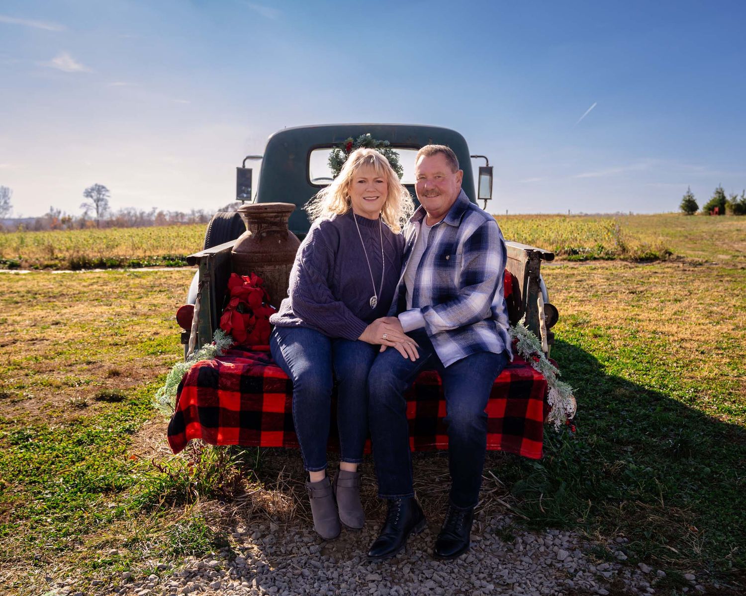 Smiling couple sitting together on the tailgate of a vintage truck in a sunny farm field.