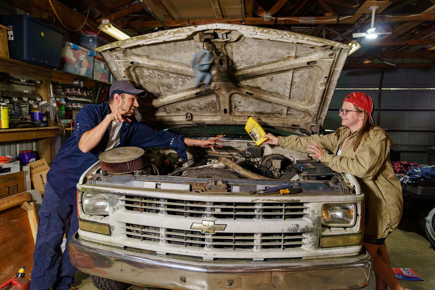 Couple working together under the hood of a classic Chevrolet truck in a vintage garage.