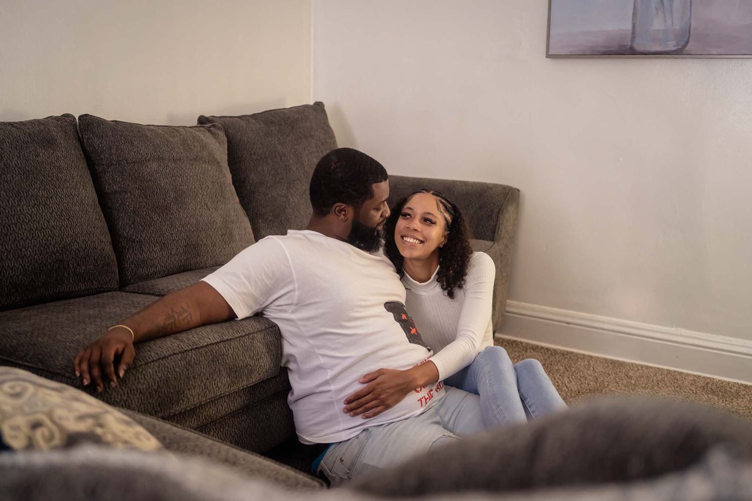 Romantic couple sharing a tender moment leaning against a gray sofa on the living room floor.