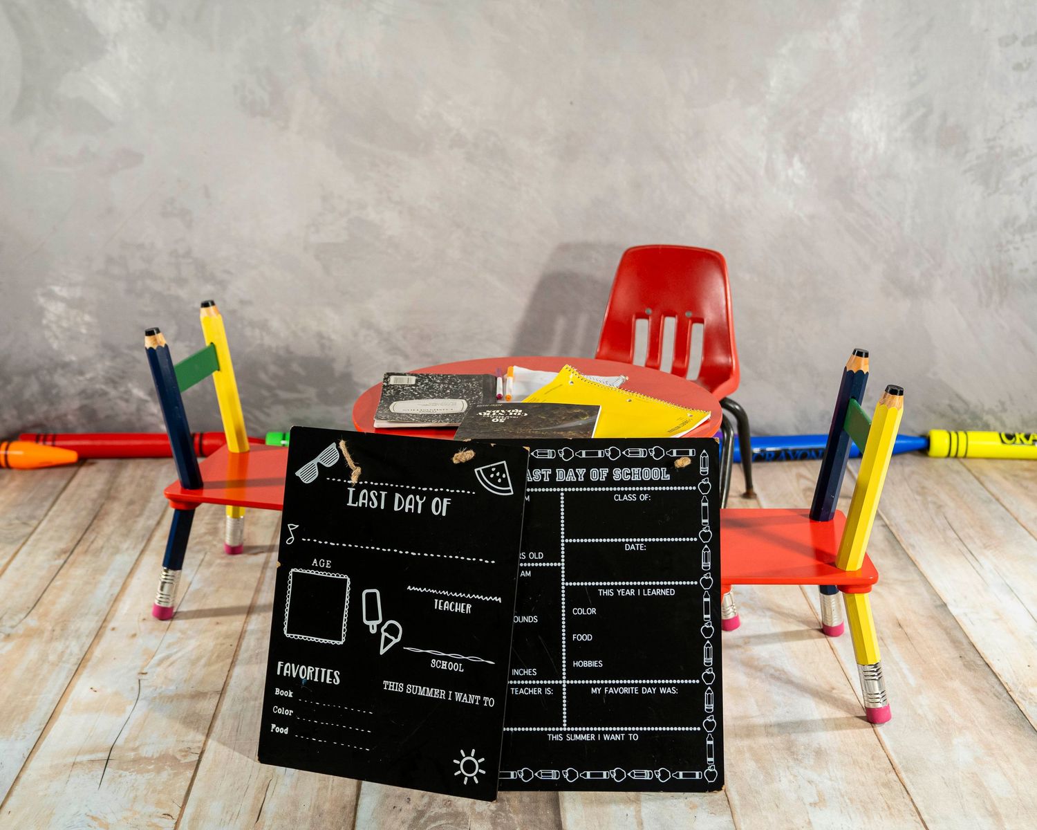 Red school desk with last day of school chalkboard sign, colorful pencils, and crayons on gray background.
