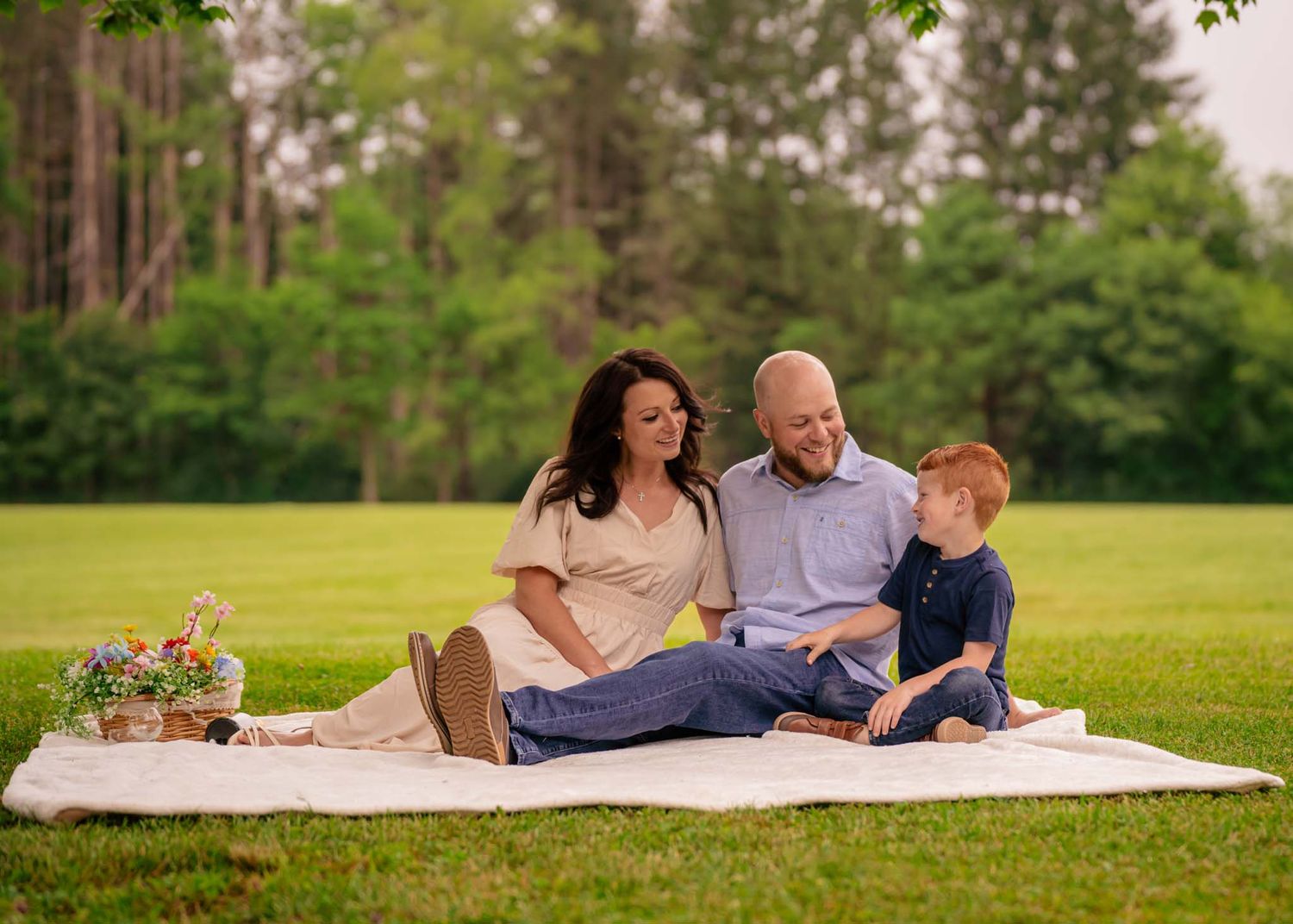 Happy family of three enjoying a picnic on white blanket in park.