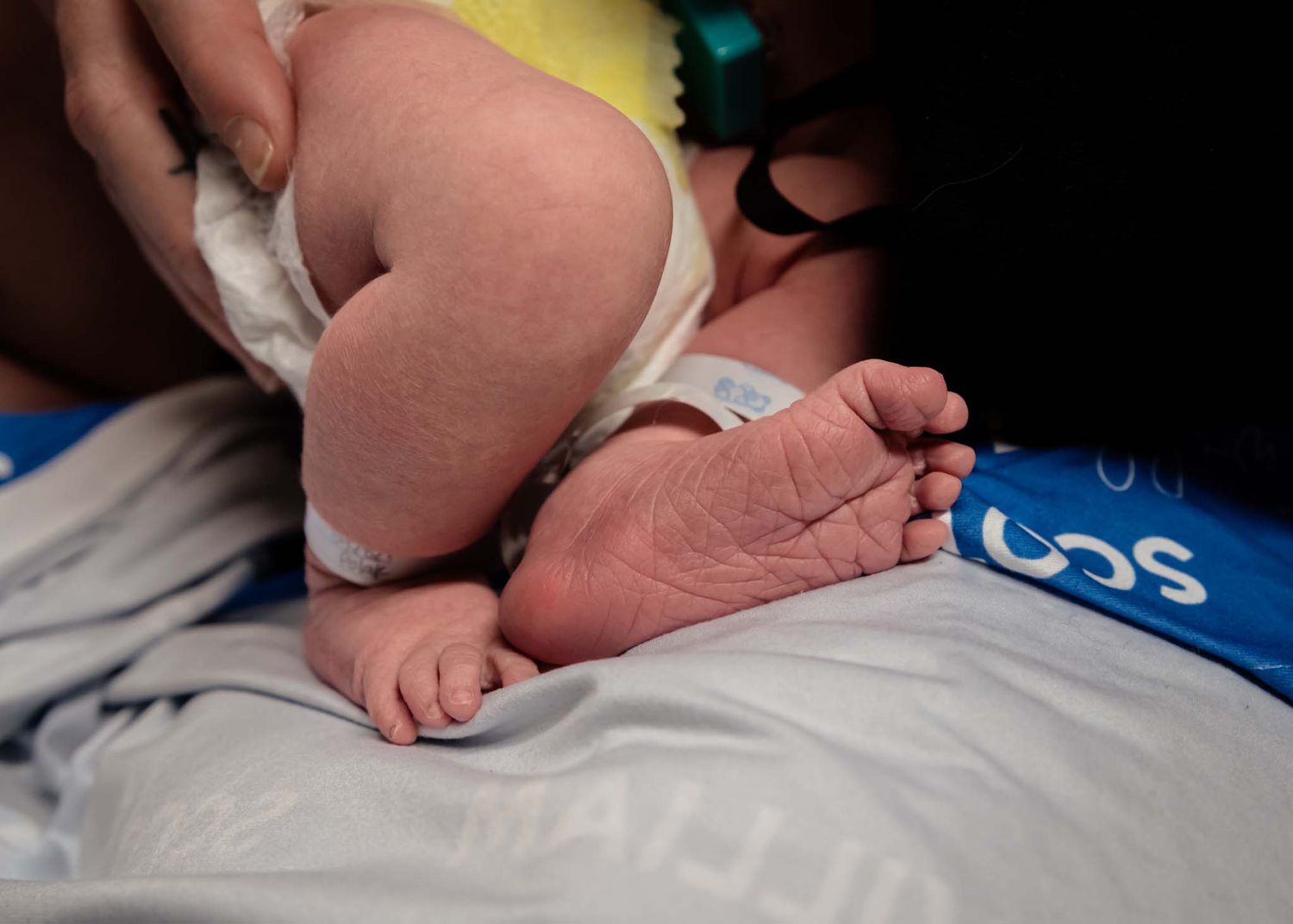 Close-up of newborn baby tiny feet and legs resting on blue personalized swaddle blanket in hospital.